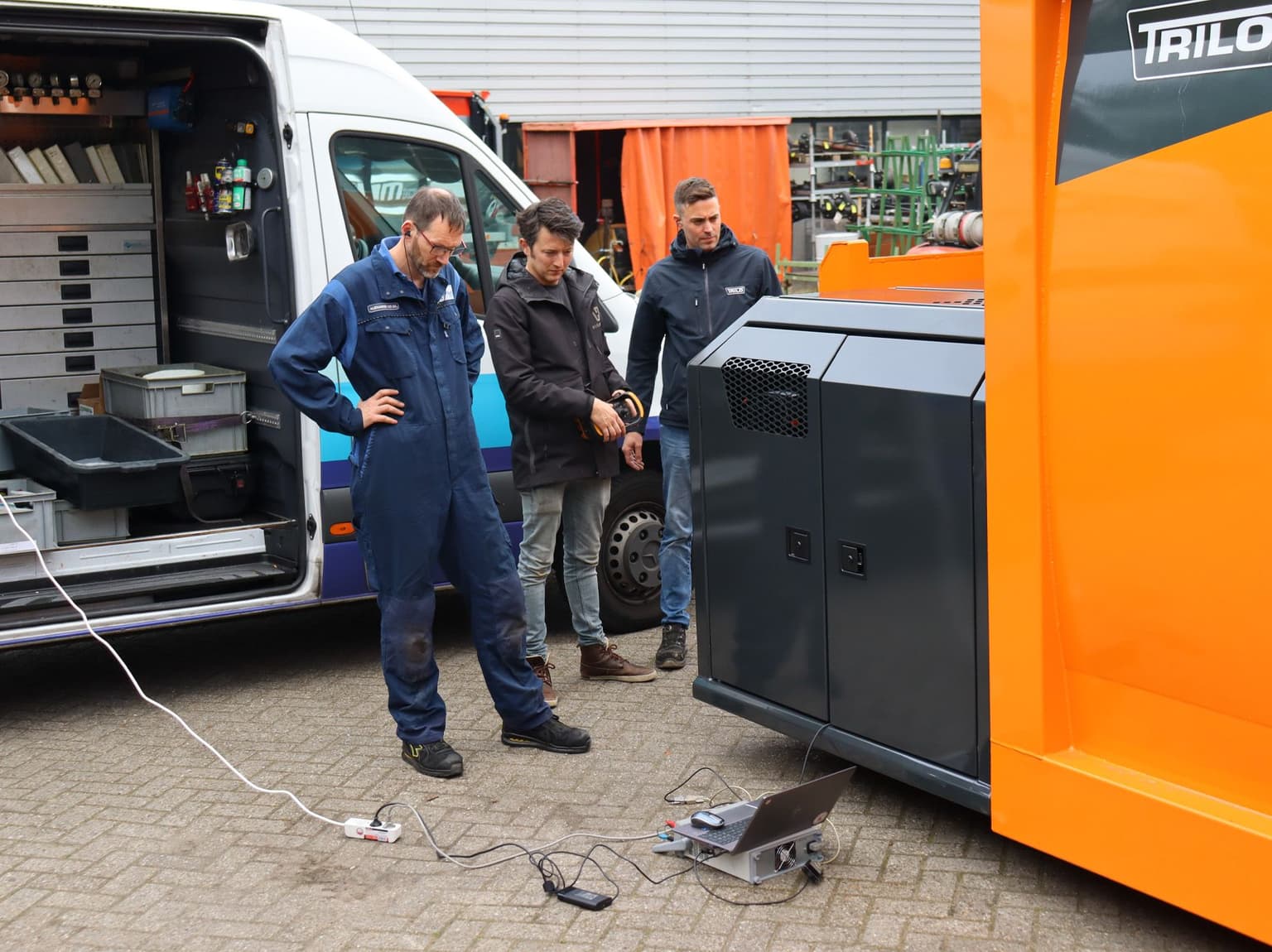 Techniker arbeiten an der hydraulischen Antriebsanlage eines Trilo TX Vacuum Containers neben einem Servicefahrzeug.